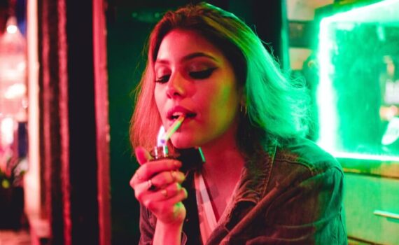 Młoda dziewczyna podpala papierosa w barze z neonowymi światłami
